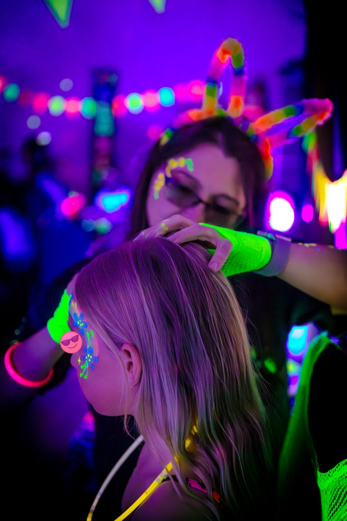 Jaime from Treasure Box Parties painting a guest's face with UV designs at Darcie’s Glow Disco birthday party in Bagshot. Offering professional UV face painting for children’s parties in Bagshot and surrounding areas.