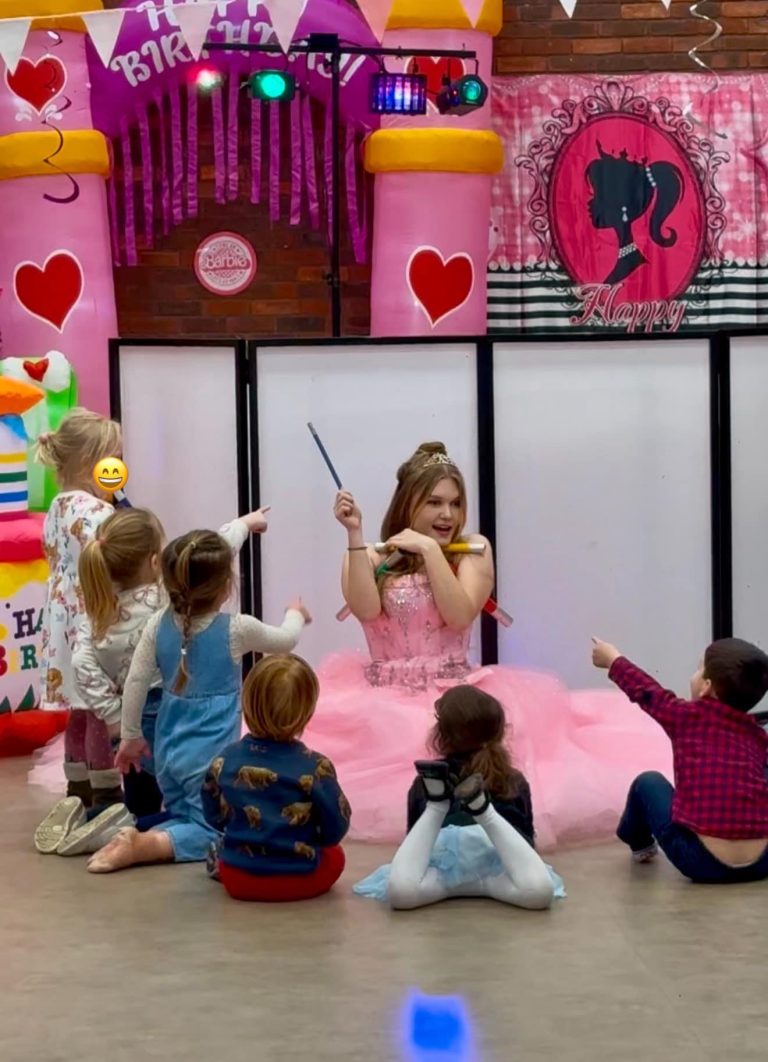 Barbie entertainer in a pink gown with children seated around her in front of a Barbie setup