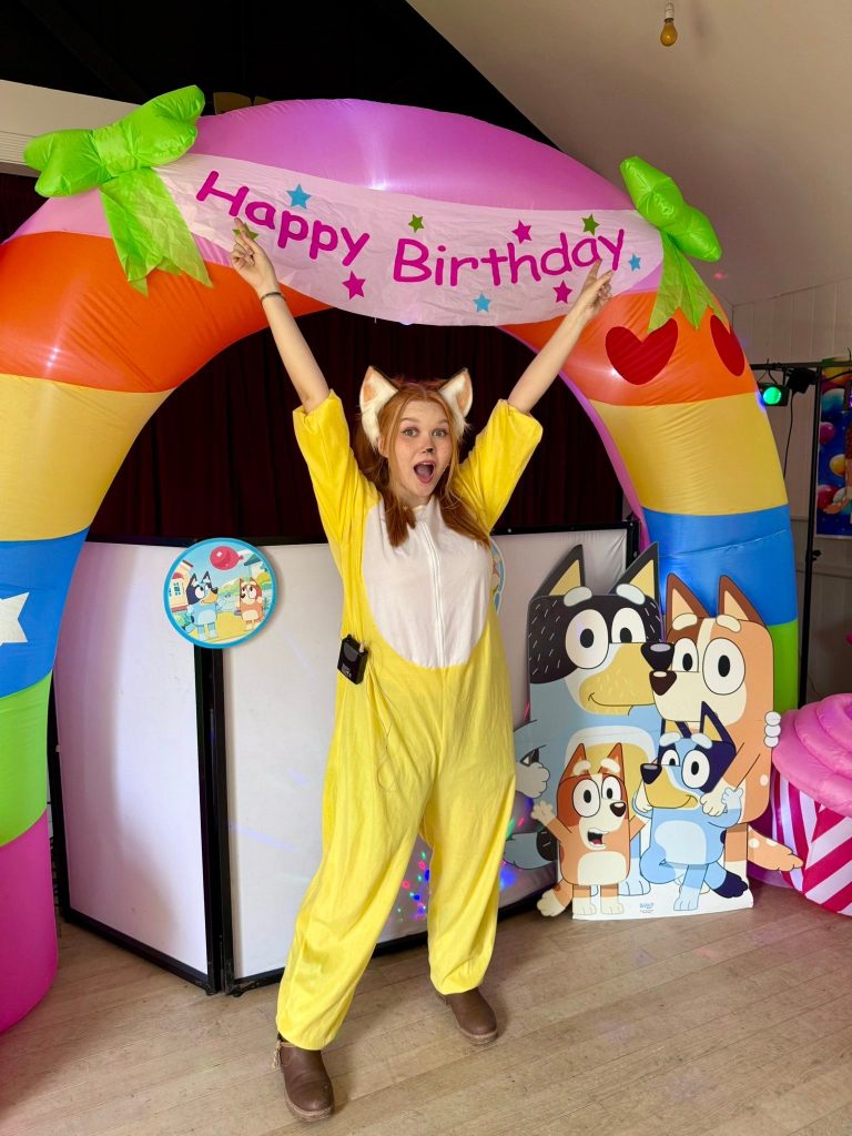 Entertainer cheering under a rainbow birthday arch beside Bluey family cut-outs