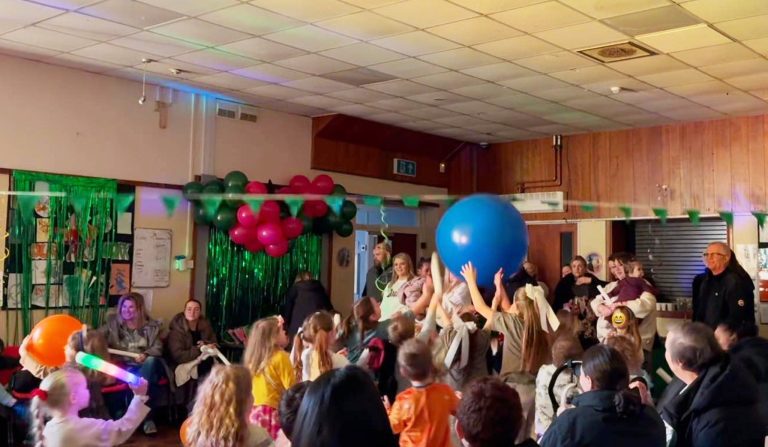 Children reaching for a giant blue balloon in a decorated hall