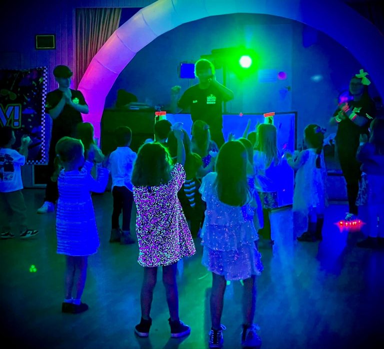 Children dancing under UV light in front of a glowing arch at a glow disco