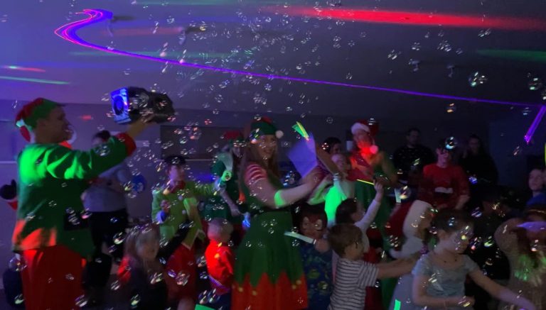 Christmas elves blowing bubbles at children during a glow disco