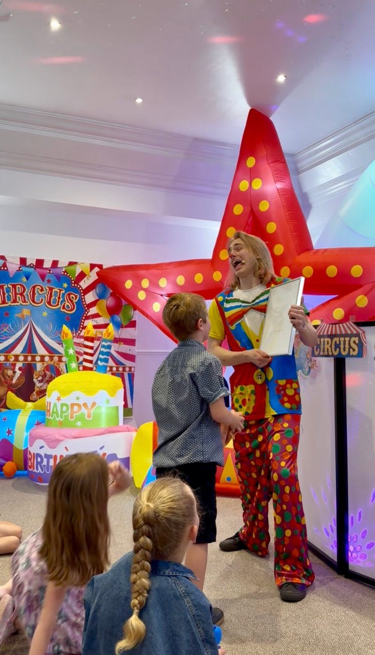 Clown entertainer performing magic for children in front of circus decorations