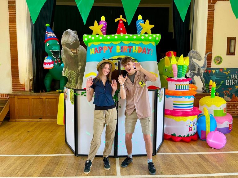 Two dinosaur explorer entertainers with a T-rex and dinosaur inflatables beside the DJ booth
