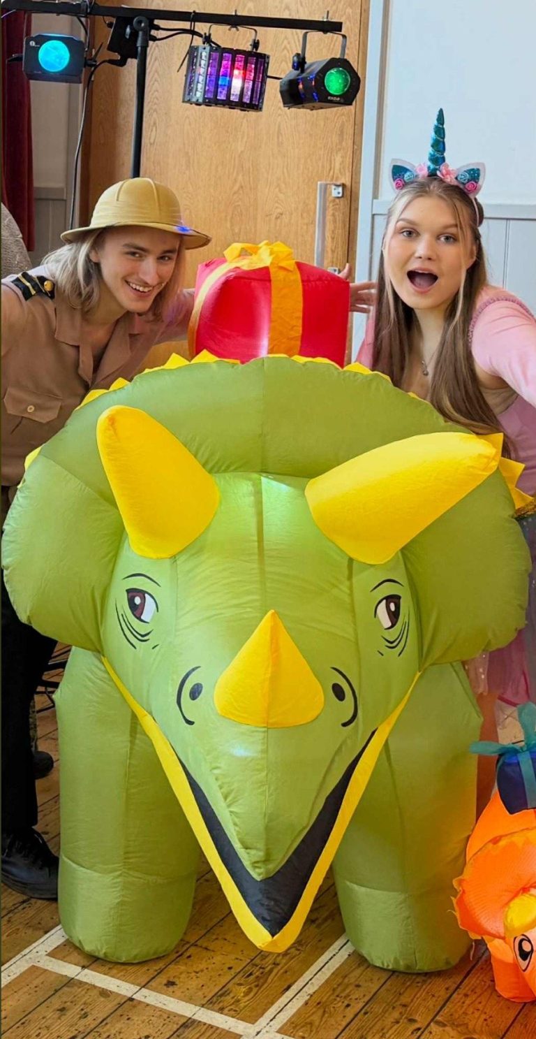 Explorer and unicorn entertainers behind a giant triceratops inflatable