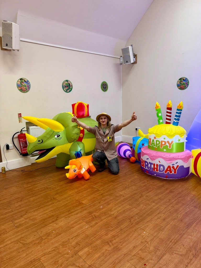 Explorer entertainer celebrating between triceratops and cake inflatables
