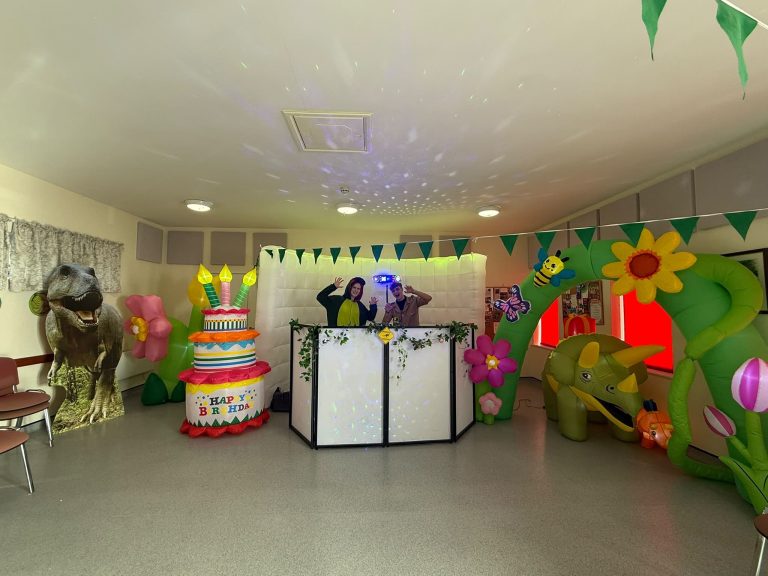 Dinosaur party setup with a jungle arch, dinosaur inflatables and lit DJ booth