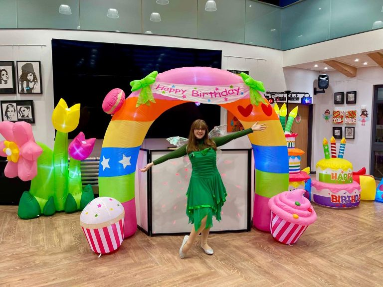 Fairy entertainer in green under a rainbow flower arch with cupcake inflatables