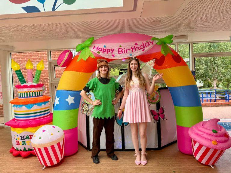Fairy and elf entertainers in front of a rainbow arch with cupcake inflatables
