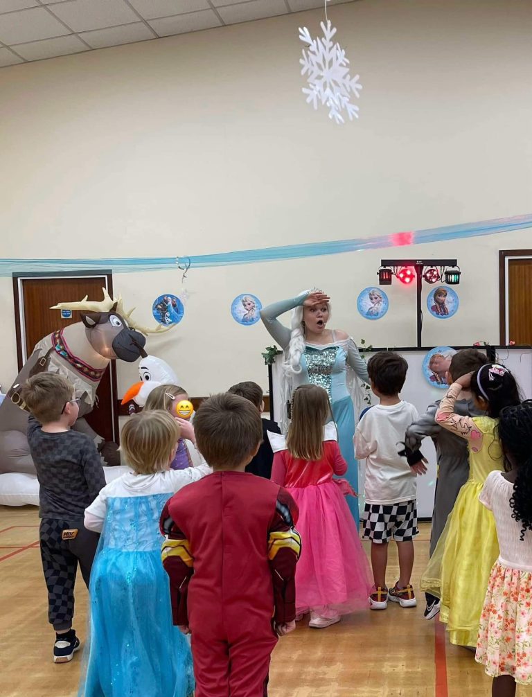 Elsa leading party games with children in costumes beside Sven and Olaf decorations