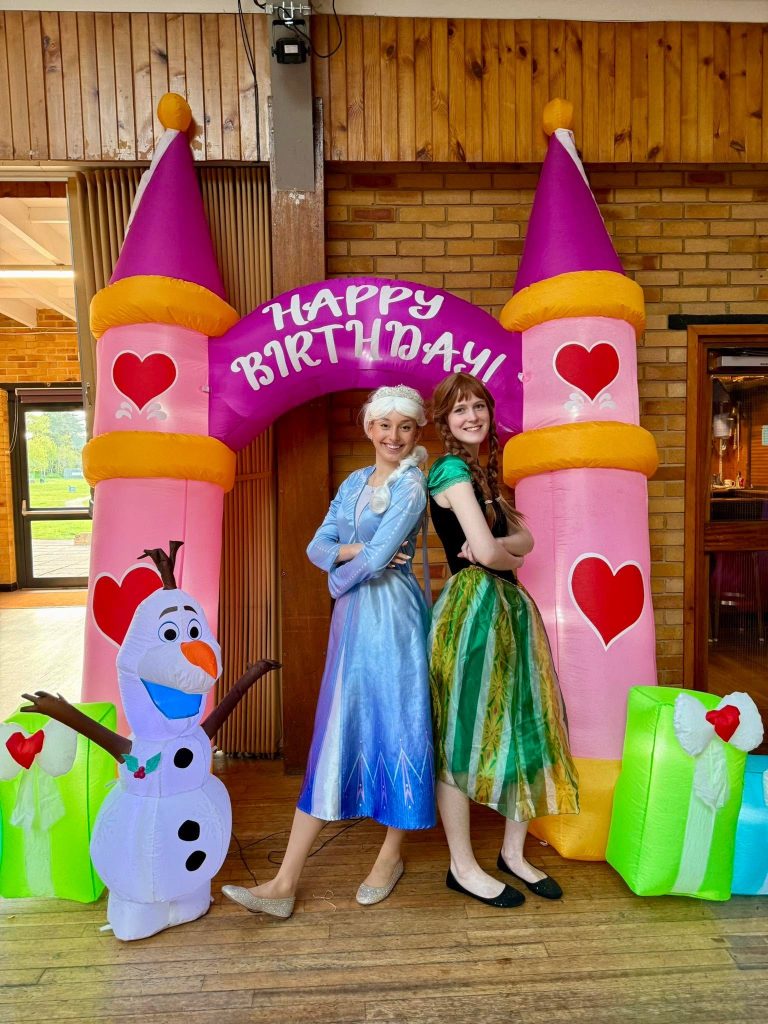 Elsa and Anna characters in front of a pink castle arch with an inflatable Olaf