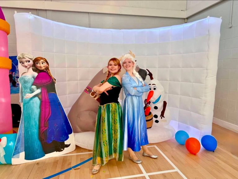 Elsa and Anna entertainers with Frozen character cut-outs in a village hall