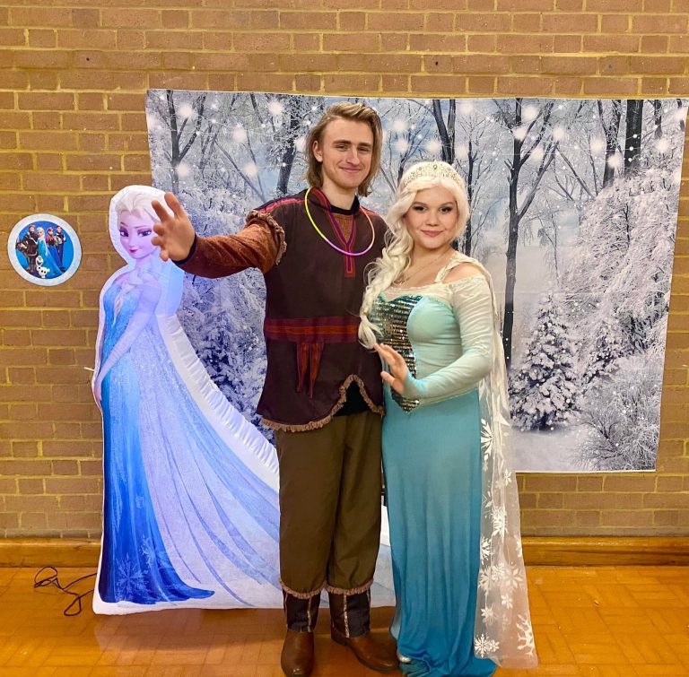 Elsa and Kristoff entertainers in front of a snowy forest backdrop with an Elsa cut-out