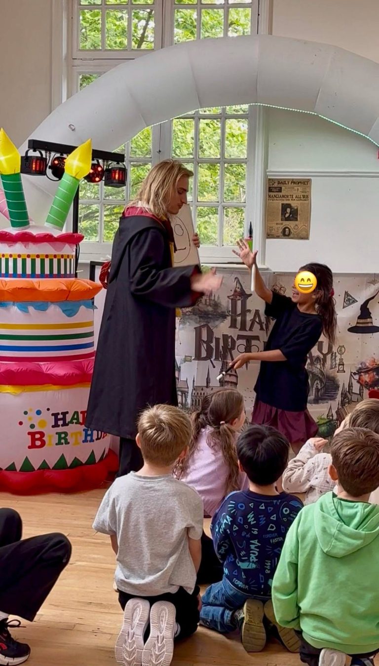 Wizard entertainer in robes performing for children seated in front of a giant cake