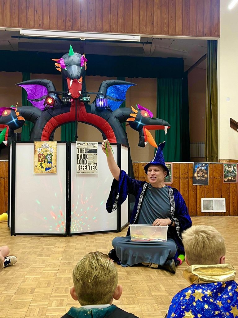 Wizard entertainer sitting in front of a dragon arch telling a story to children