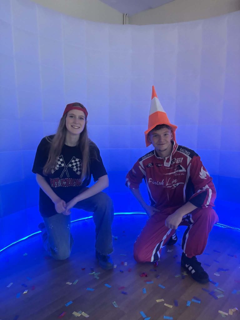 Two racing driver entertainers in racing suits crouching in a lit party booth