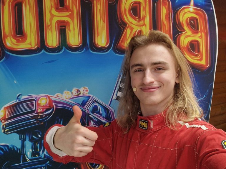 Racing driver entertainer giving a thumbs up in front of a monster truck birthday backdrop