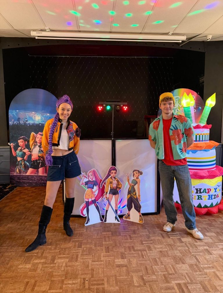 Two K-Pop entertainers beside the DJ booth with a giant birthday cake inflatable and character cut-outs