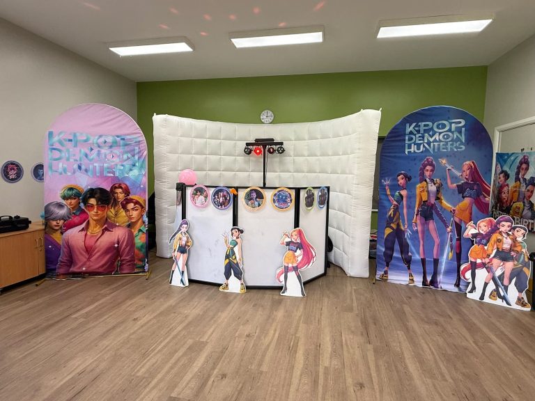 K-Pop Demon Hunters party setup with themed backdrops, character cut-outs and a lit DJ booth