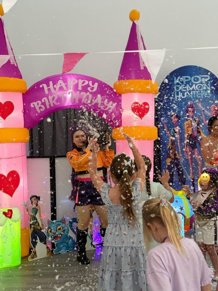K-Pop entertainer dancing under a confetti shower at a pink princess castle arch