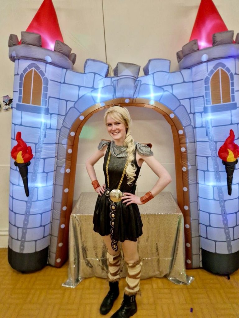 Viking style entertainer in braids and leather costume in front of a castle arch