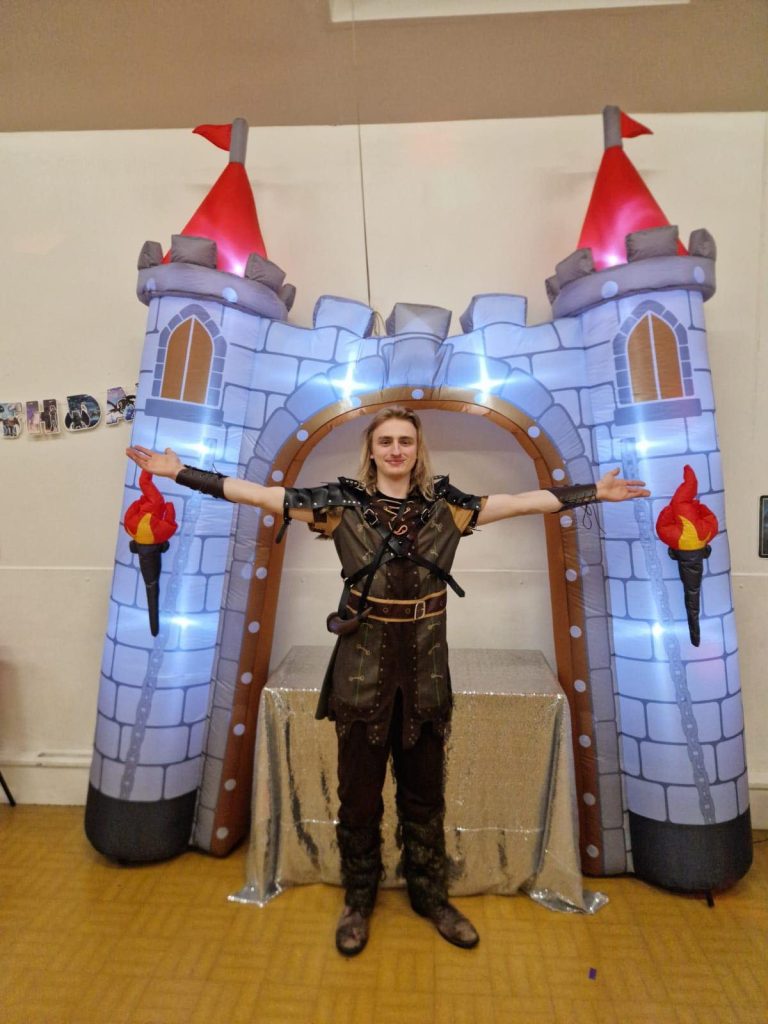 Viking style entertainer with arms outstretched in front of a lit castle arch