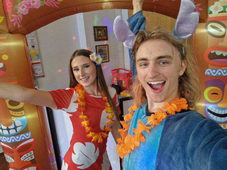 Lilo and Stitch entertainers selfie with flower leis in front of a tiki arch