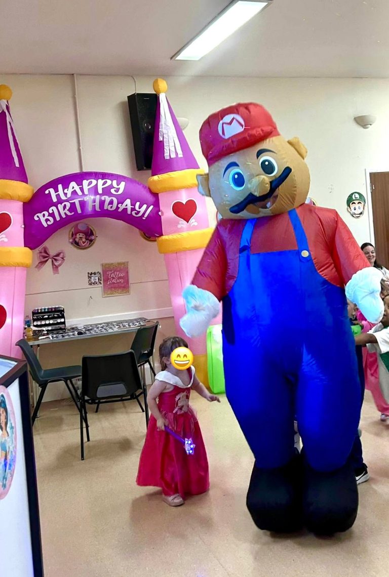 Giant Mario mascot dancing with children beside a princess castle arch
