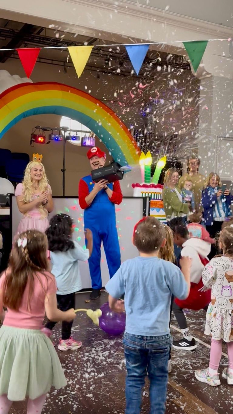 Mario and Princess Peach entertainers dancing as confetti falls under a rainbow arch