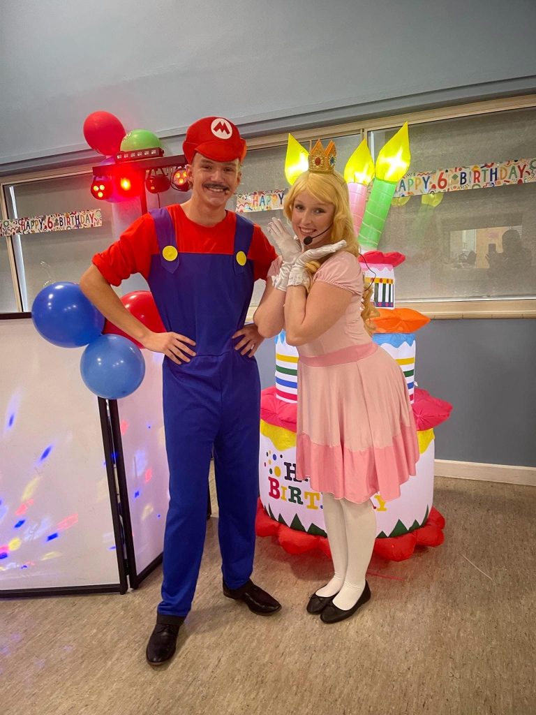 Mario and Princess Peach entertainers beside a birthday cake inflatable