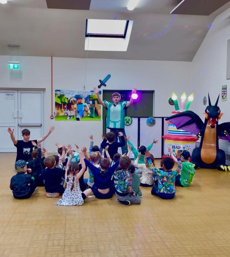 Steve entertainer leading children with arms raised in front of Minecraft decorations