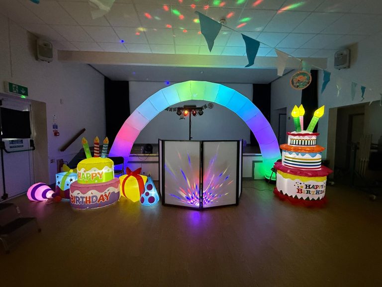 Light-up rainbow arch and cake inflatables around the DJ booth