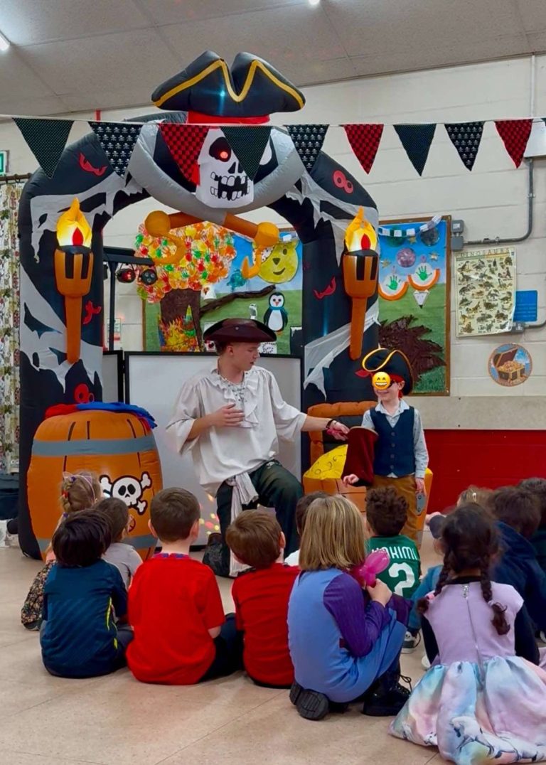 Pirate entertainer performing magic to children seated in front of the pirate arch