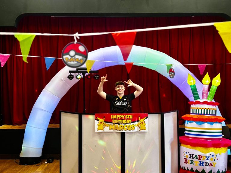 Entertainer at the DJ booth under a Pokeball arch with birthday cake inflatable