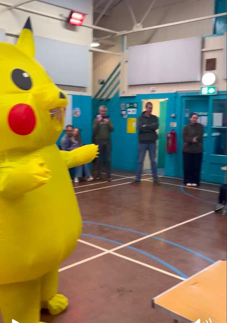 Giant Pikachu mascot waving in a sports hall