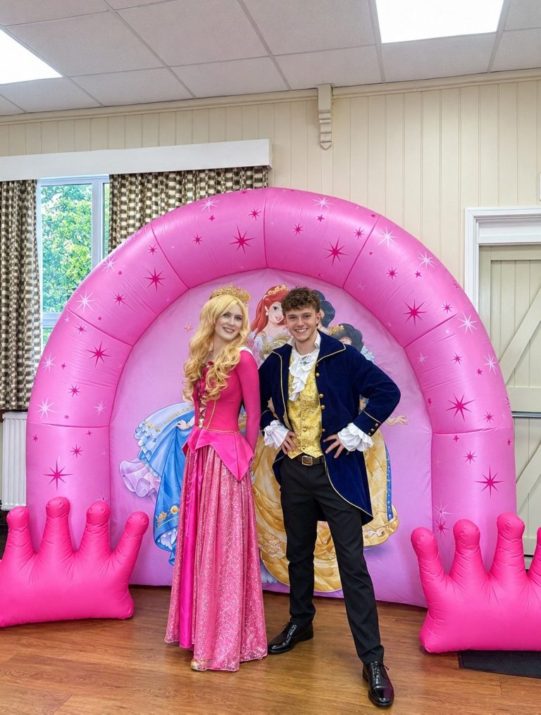 Aurora entertainer and a prince in front of a pink crown arch decorated with princesses