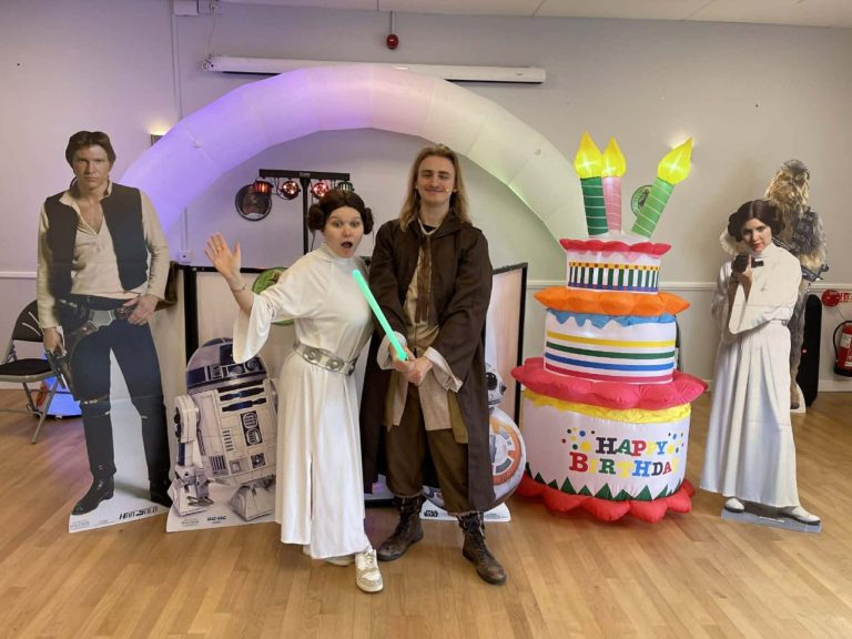 Princess Leia and a Jedi entertainer with lightsaber beside R2-D2 and a cake inflatable