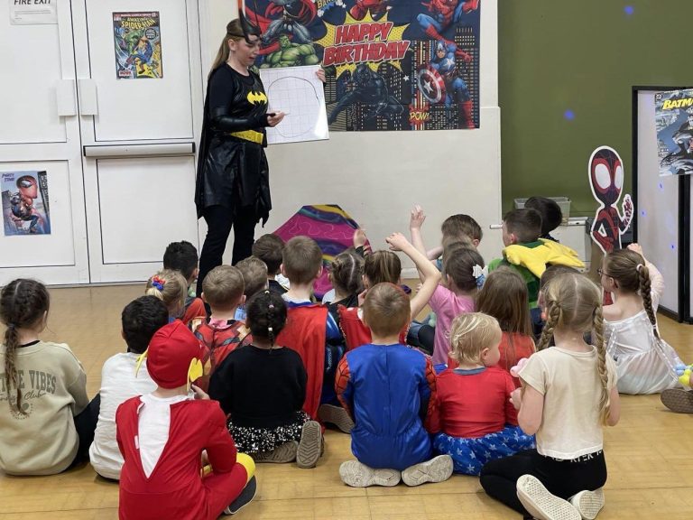 Batgirl performing a magic show for children in superhero costumes