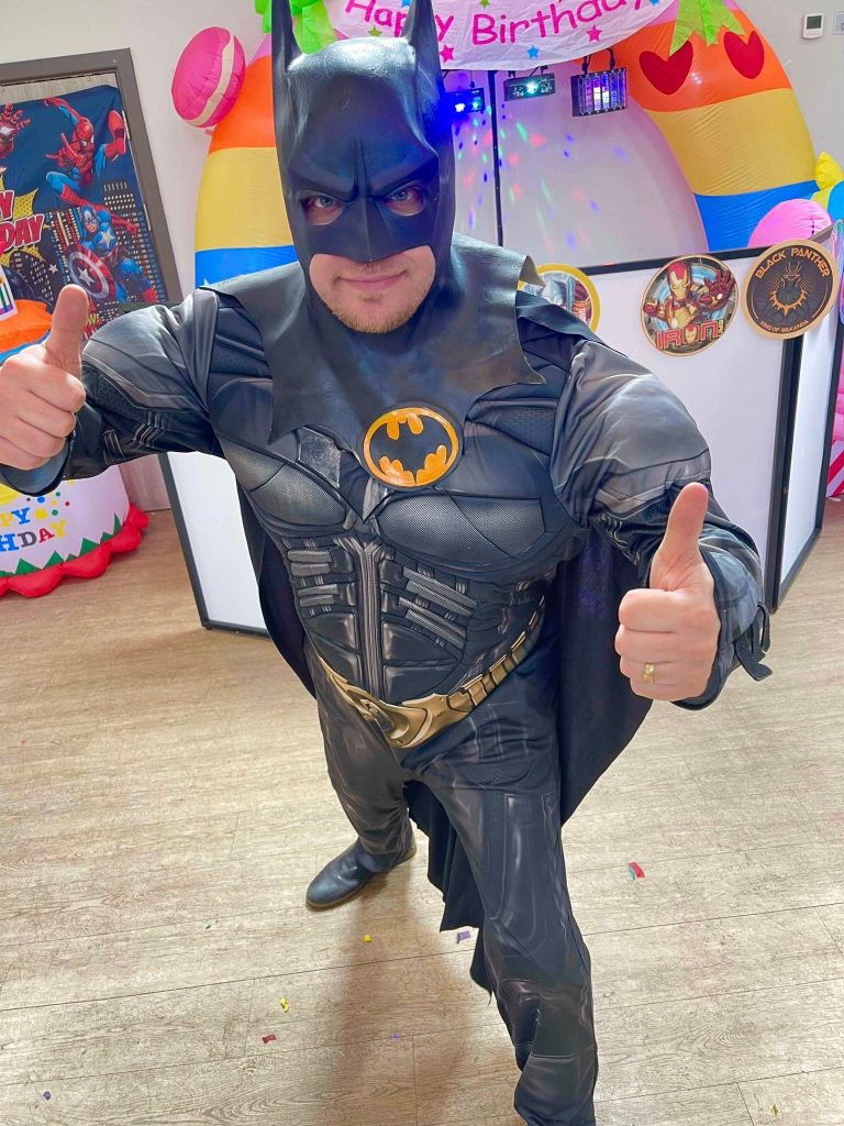 Batman entertainer giving two thumbs up beside a birthday arch