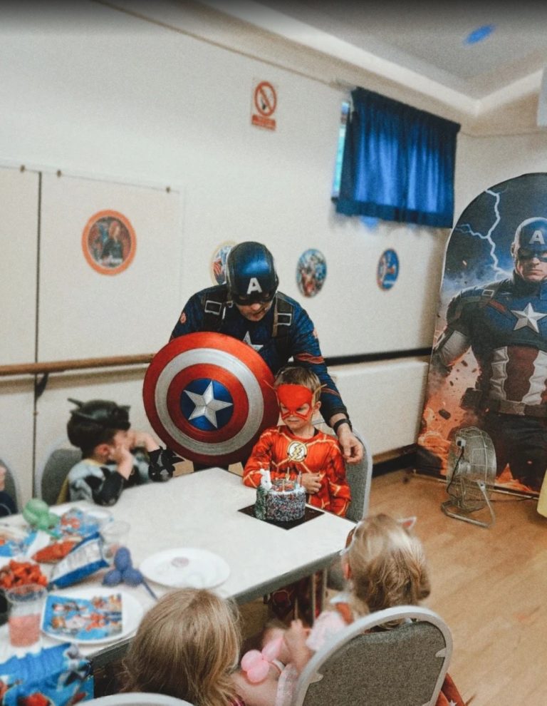 Captain America entertainer with his shield sitting with children at the party table