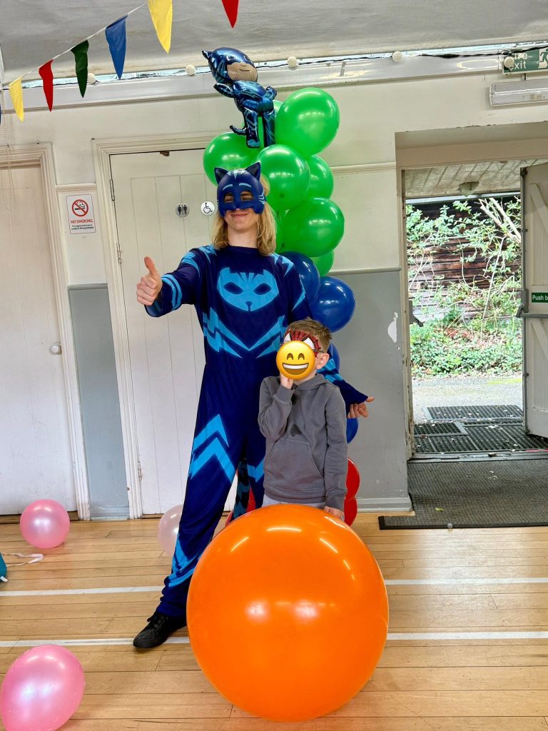 Catboy entertainer in blue with a giant orange balloon and balloon decorations