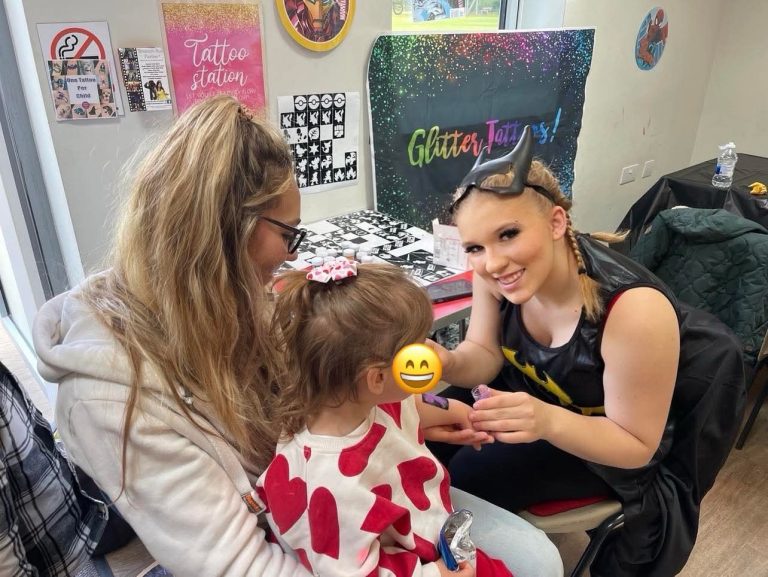 Face painter in a Batgirl costume painting a young child's face