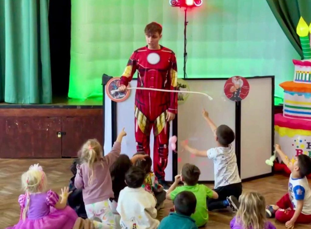 Iron Man magic show - Treasure Box Parties Iron Man entertainer performing a trick for children sitting on the floor