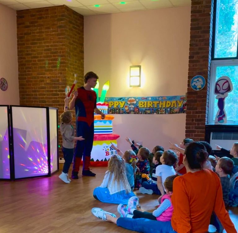 Spider-Man entertainer performing a magic show to children beside a birthday cake inflatable