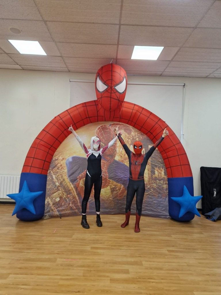 Spider-Man and Ghost-Spider entertainers with arms raised under a Spider-Man arch