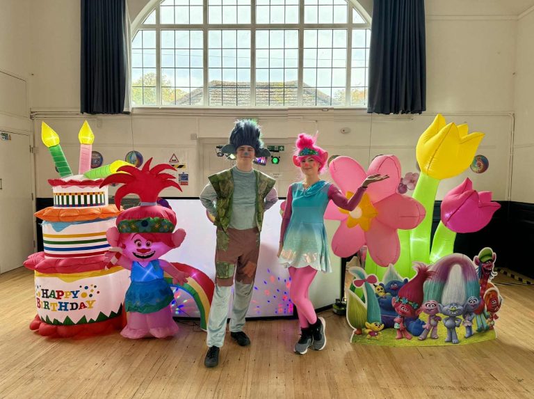 Poppy and Branch entertainers in a Trolls party setup with flower inflatables