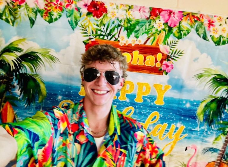Tropical entertainer in a Hawaiian shirt and sunglasses in front of an Aloha backdrop