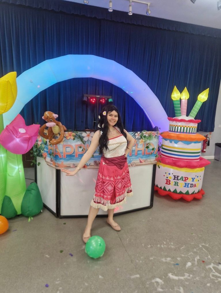 Moana entertainer under a rainbow light-up arch with a tropical flower inflatable