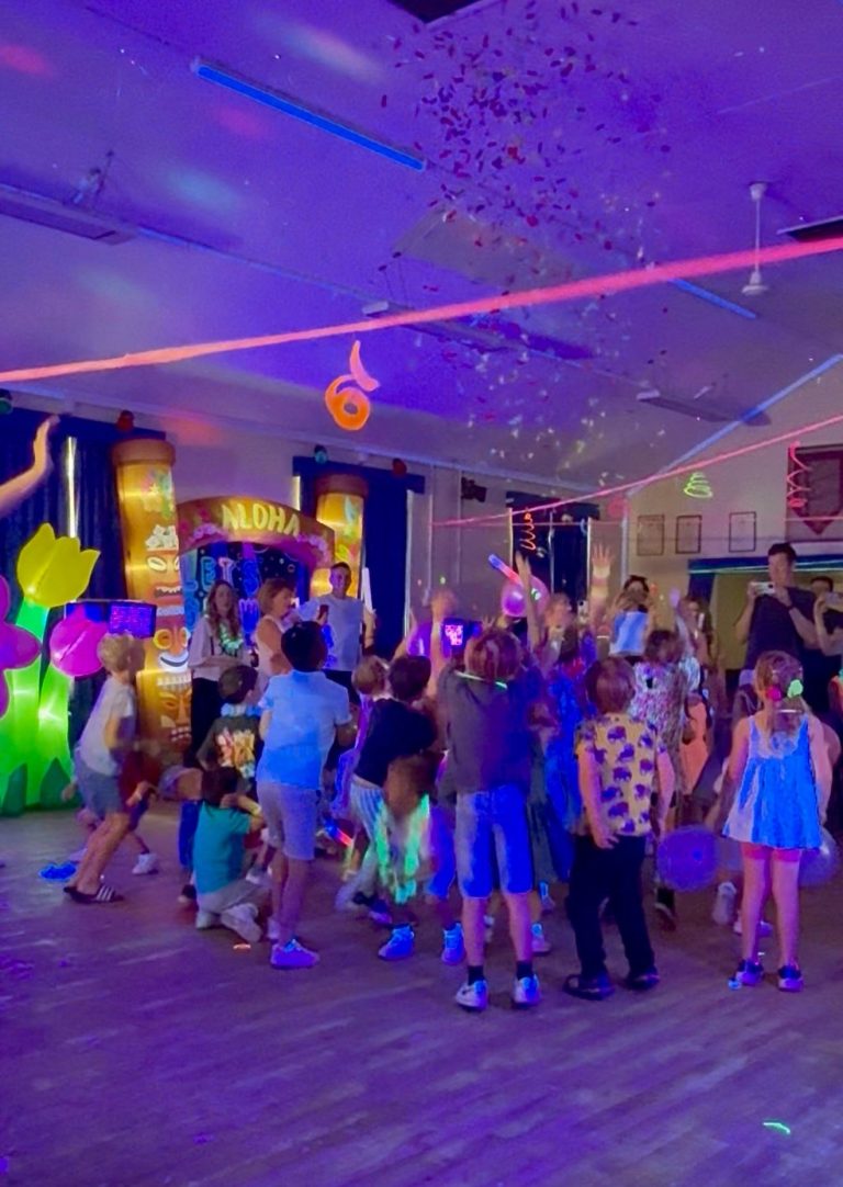 Tropical glow party with children dancing between glowing palm and tiki decorations