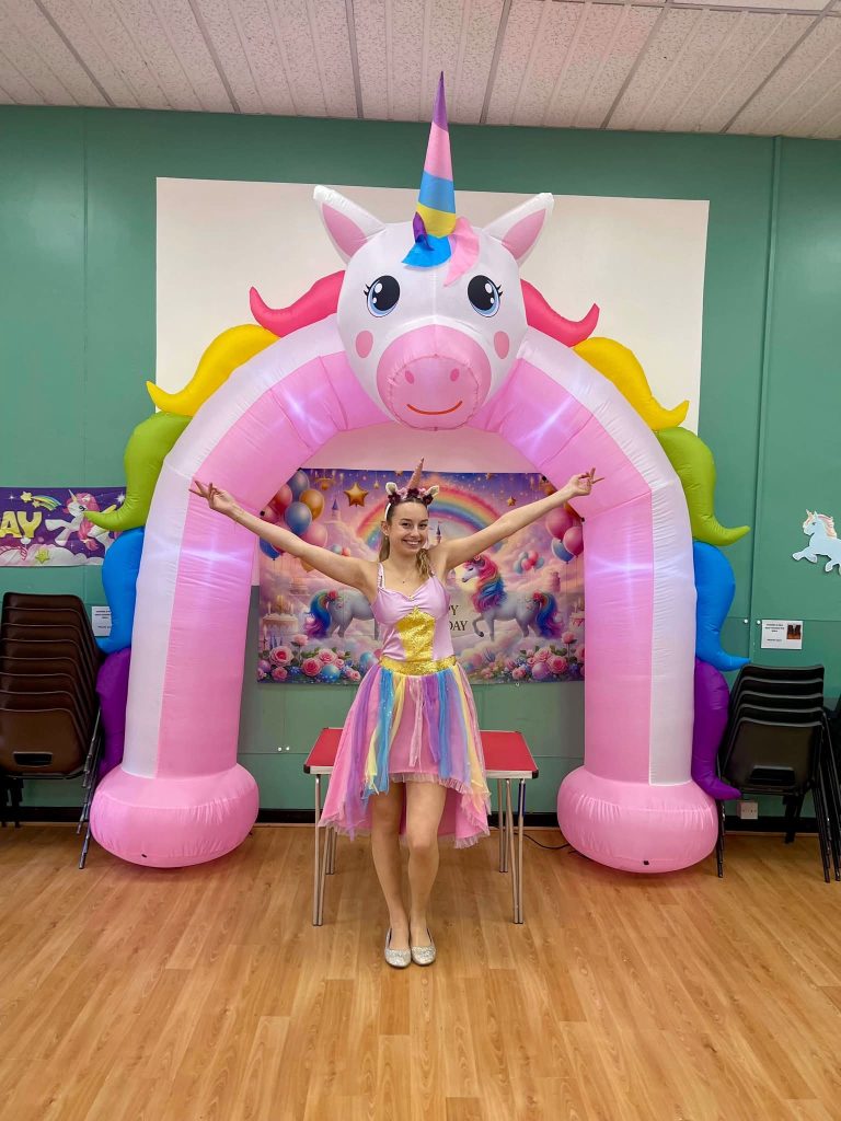 Unicorn entertainer with arms wide under a giant pink unicorn arch